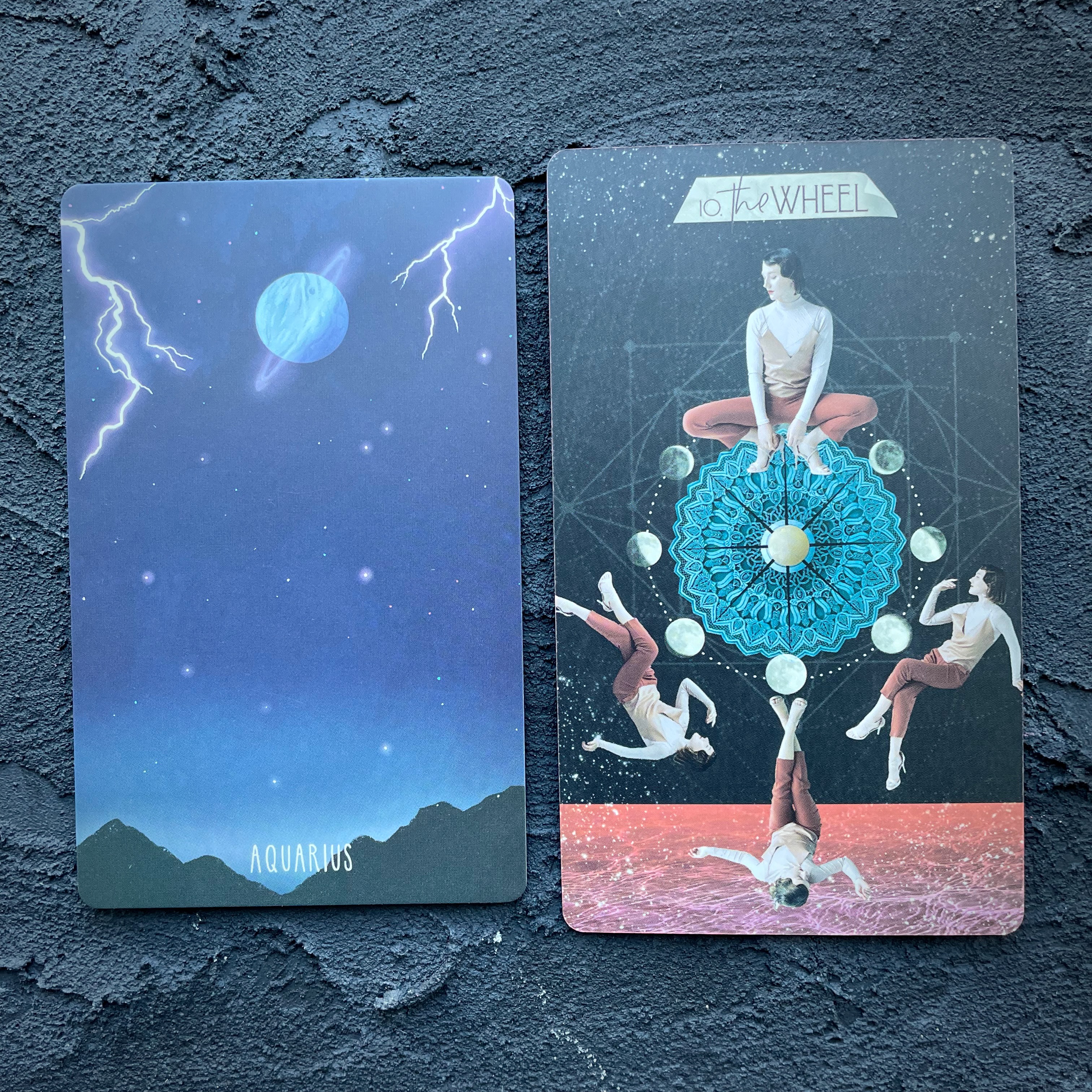 Two cards in front of a navy blue background, right to left: Aquarius (a stormy sky with Saturn rings) and the Wheel ( a circle with four people doing yoga around it)