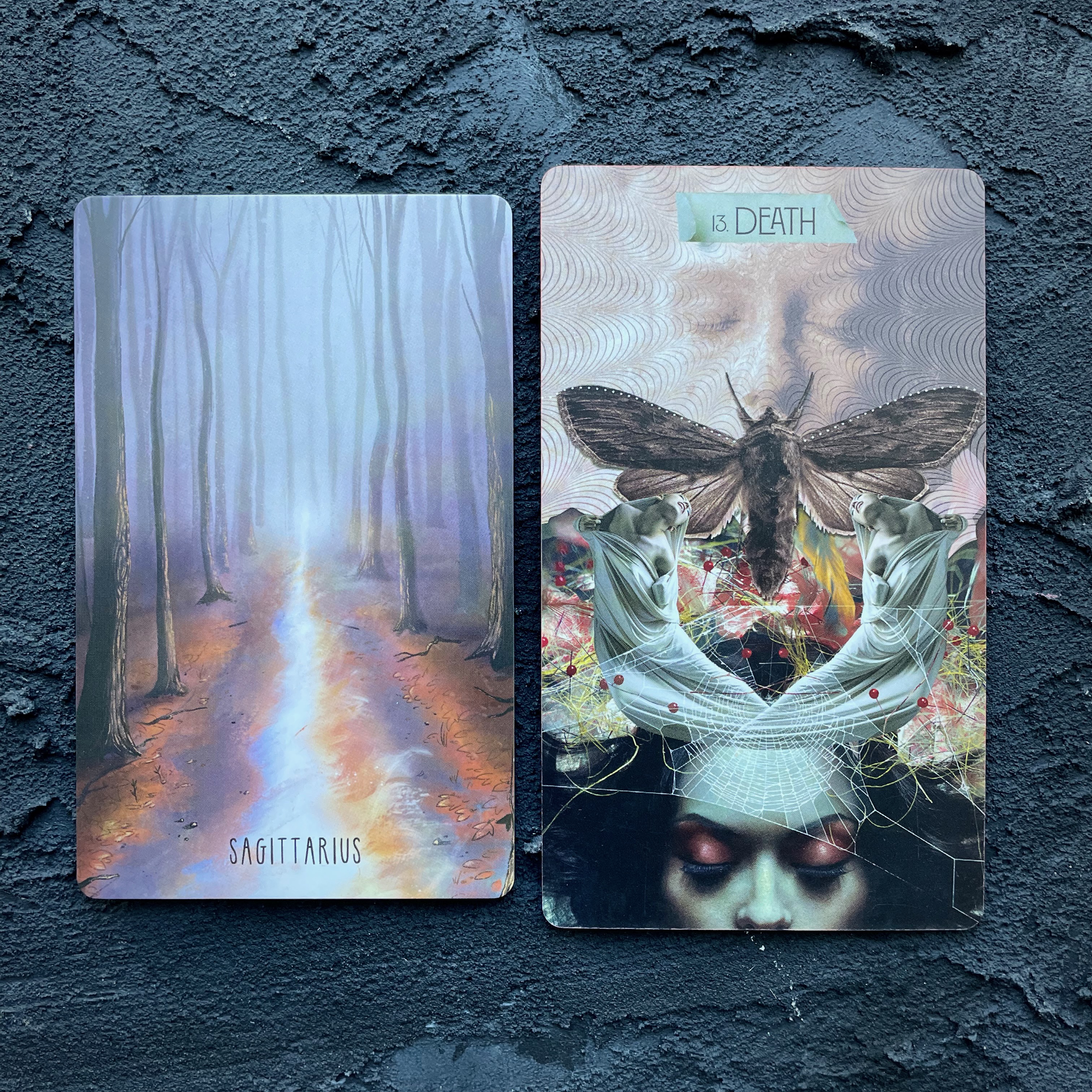 Two cards in front of a navy blue background, right to left: Sagittarius (a desolate road on a foggy fall evening) and Death (a woman with pink eyeshadow has her eyes closed and is covered by a moth and a spiderweb)
