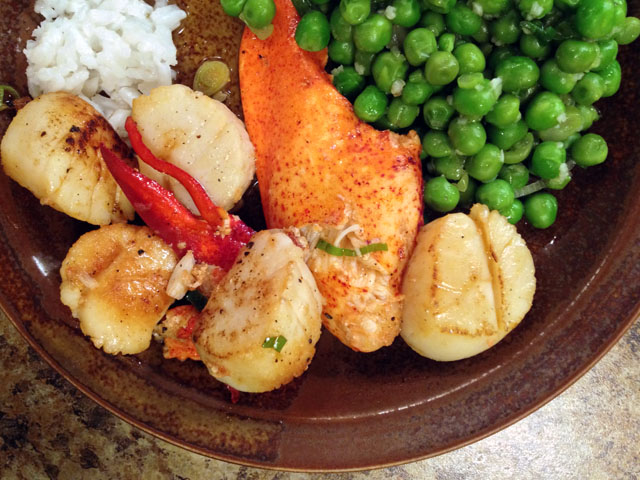 A plate of lobster pieces, scallops, rice and peas.