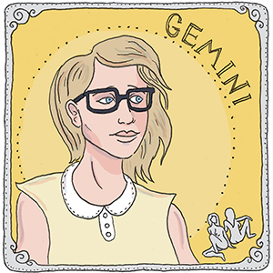 person with dark wire-rimmed glasses and blonde hair representing the star sign Gemini