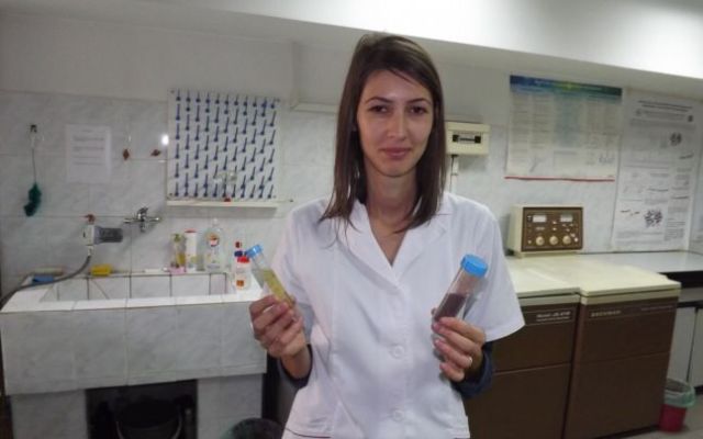 A woman holds two vials of fluid, one red, one yellow.