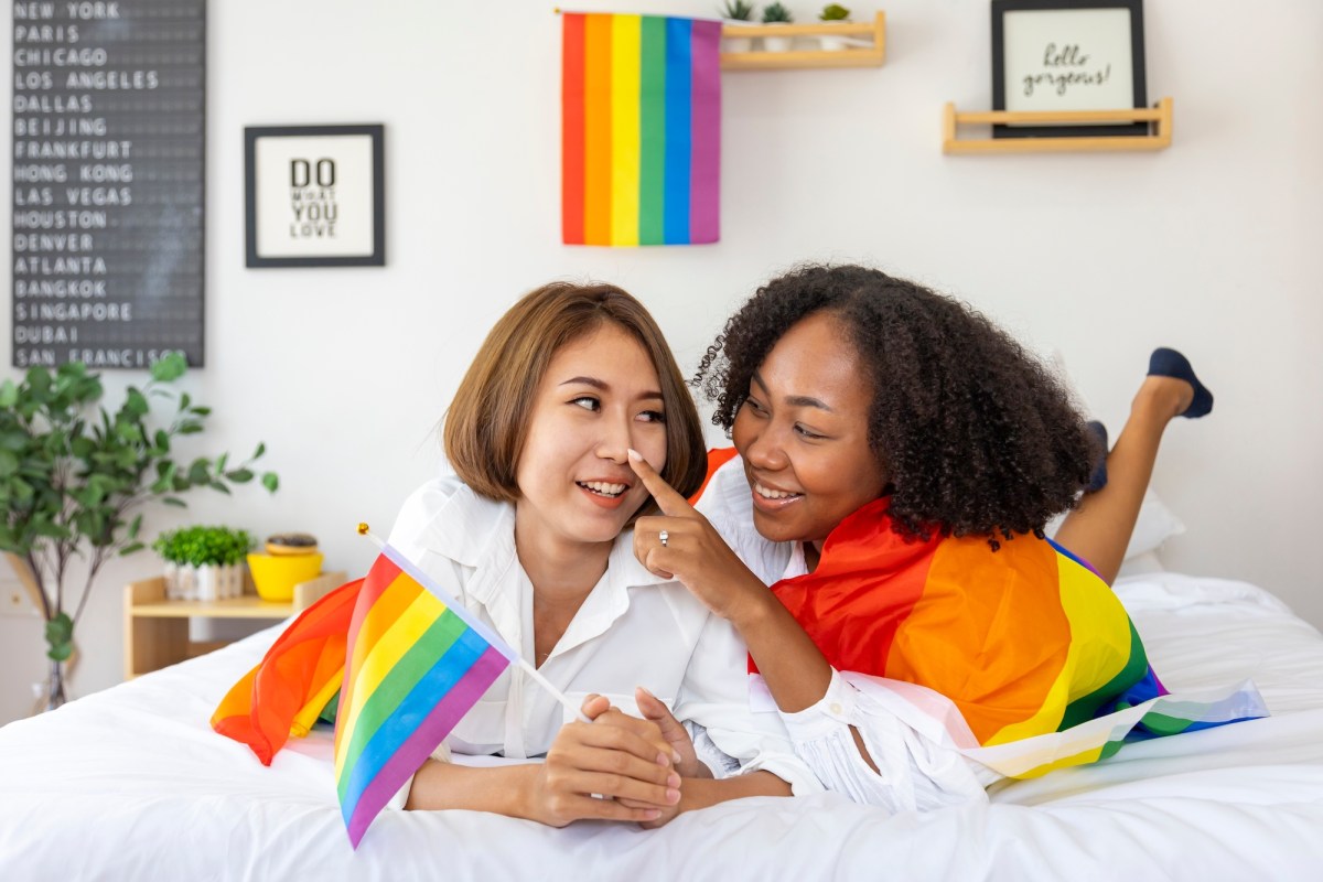 Lesbian couple in bed surrounded by rainbow flags