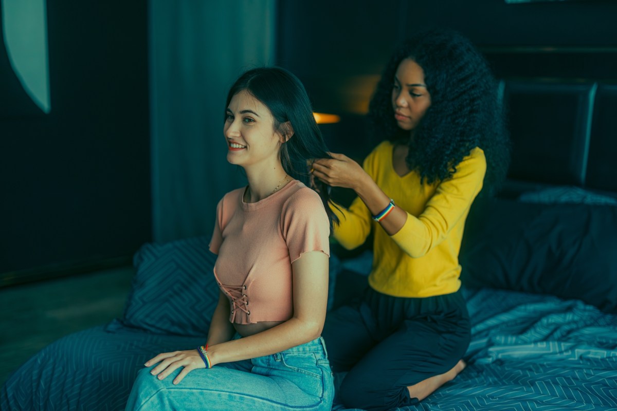 Lesbian lovers engage in playful interactions on bed as one braids the others hair