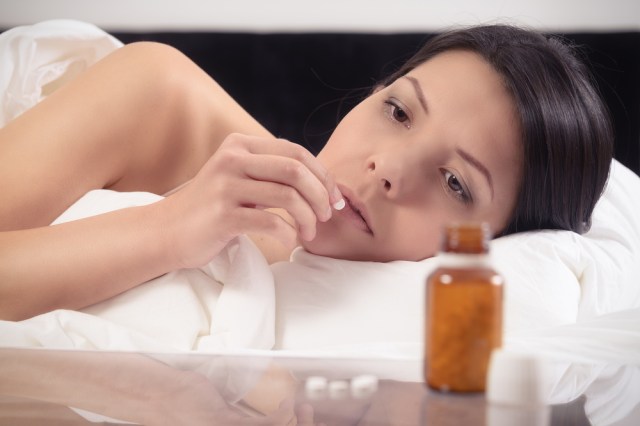 Woman looking at pill in bed.