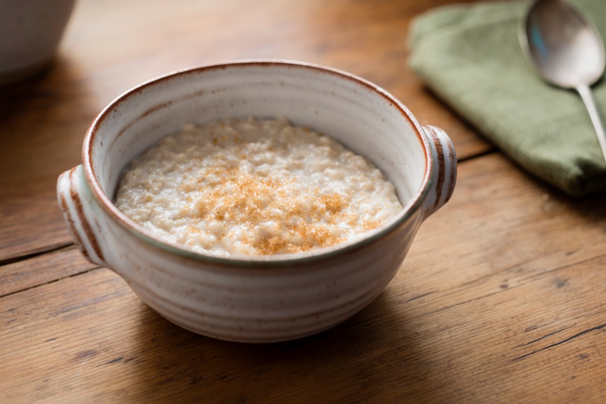 Photograph of a rustic hand made bowl filled with freshly made Porridge, topped with sprinkled Demerara sugar. Photographed on a rustic old pine rustic table.