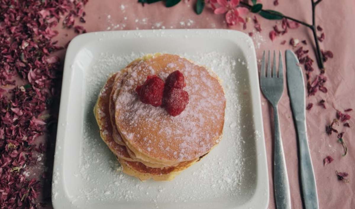 pancakes on a plate with raspberries on top, the plate is on a pink tablecloth