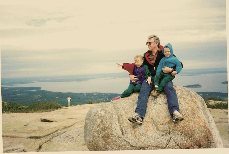 there is a man (rachel's dad) with two young children, one is Rachel, the other her sibling. They sit on a giant boulder together, the outlines of their coats animated to flash in white