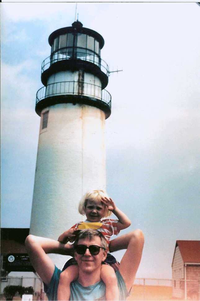 Rachel is very young in this photo, maybe three or four years, and sits on her dad's shoulders in front of a lighthouse. there are animated white lines around her person that flash.