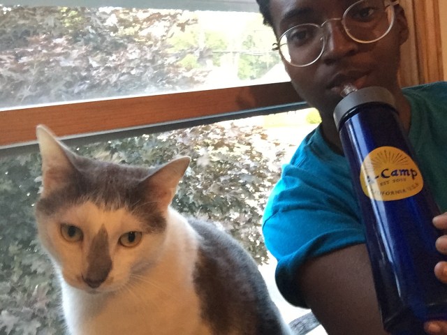 Alaina drinking from her A-Camp water bottle with her cat Alexei.