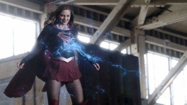 Kara flying and smiling while being hit by laser beams.