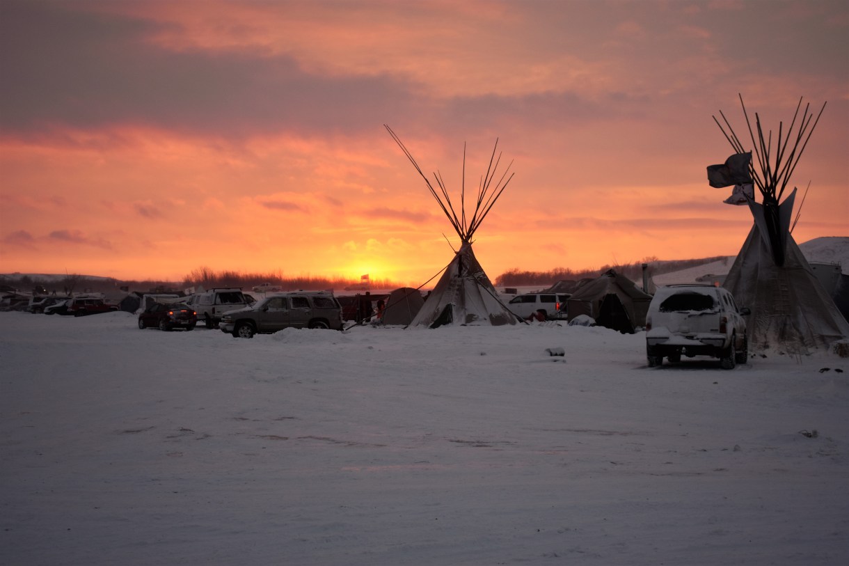 Cars and teepees in front of a sunset. Oceti Sakowin encampment, December 5, 2016. Photo by Jen Deerinwater. Read more coverage about DAPL resistance here.