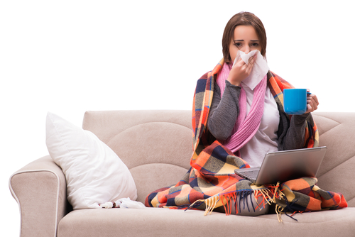 young woman sitting on a couch drinking tea and looking sick