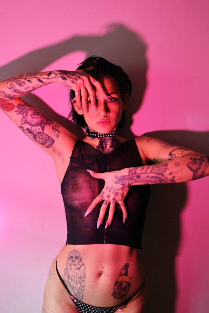 Nasty Candy, in a nipple-revealing mesh crop top and thong, lit with pink tones