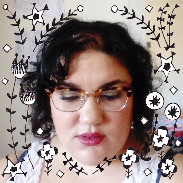 A woman in her late twenties with brown hair and skin wearing red lipstick and turtle shell glasses glances down, away from the camera. There are various animated shapes and plants around her head from a Snapchat filter.
