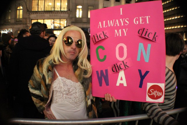 A person in a blonde wig holding a sign that says "I Always Get My Conway"