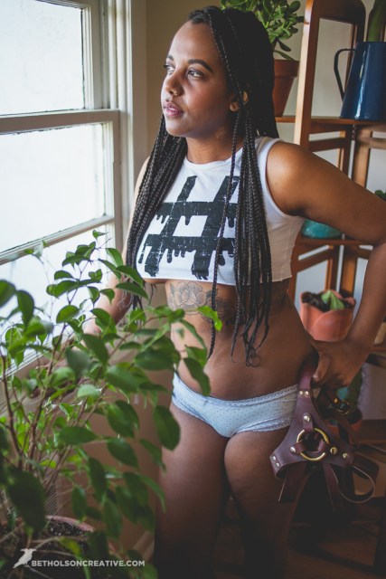 A woman in a crop top and underwear standing by a window