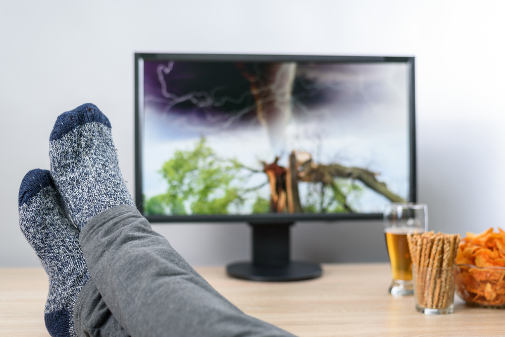 Person with legs resting on coffee table, watching a television showing an approaching tornado
