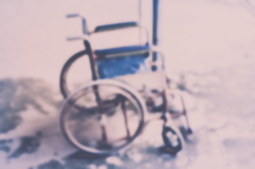 An out of focus manual wheelchair with a blue seat.