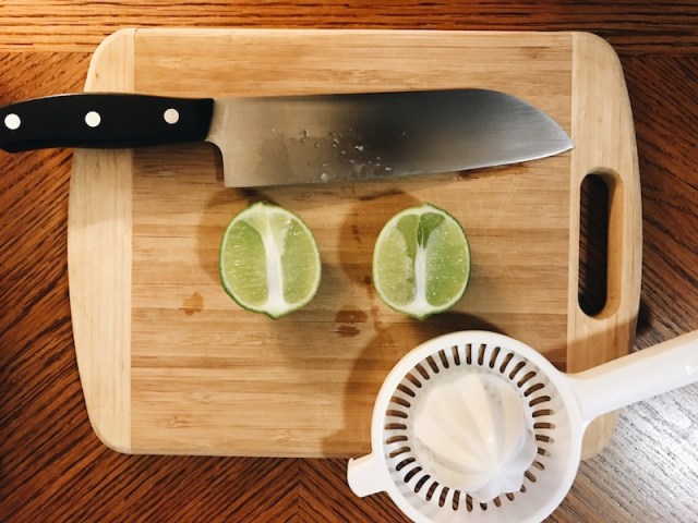 a lime, cut lengthwise, on a cutting board with a knife and a shitty juicer
