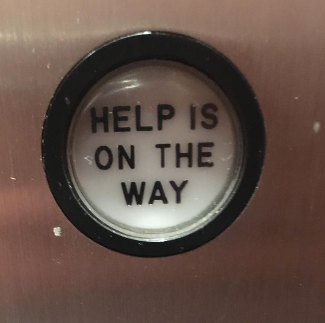 An elevator button that says "help is on the way" in black block letters.