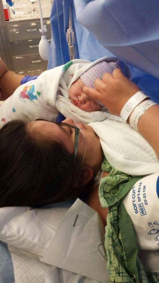 A mother holds a newborn baby in their arms in a hospital bed.