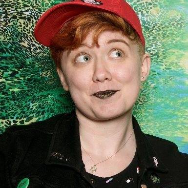 A young person with red hair and wearing a red baseball cap with dark lipstick.