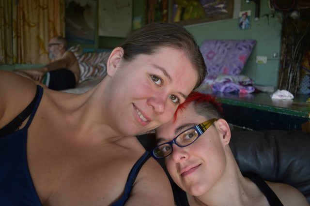 Two women, one with brown hair and one with a bright red mohawk, smile lovingly into the camera.