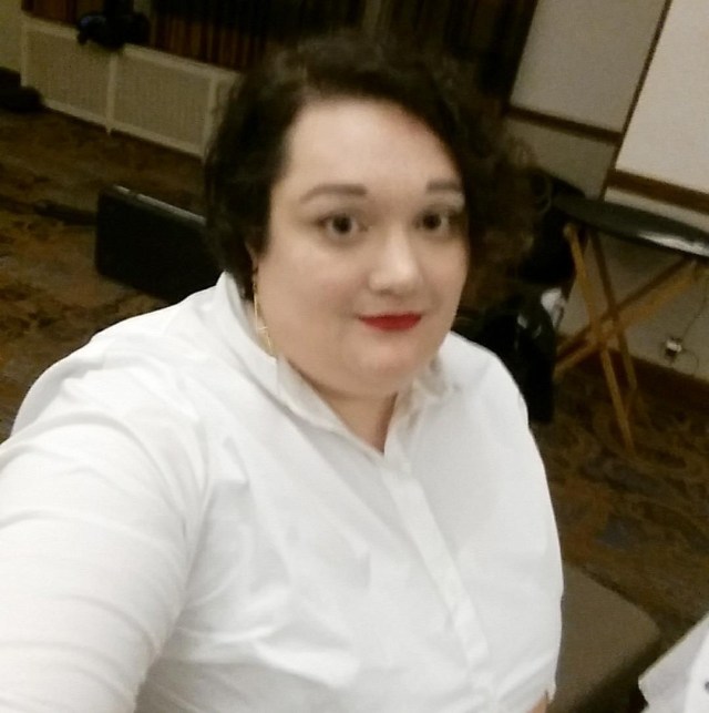 A woman wearing red lipstick and a white button down shirt takes a selfie.