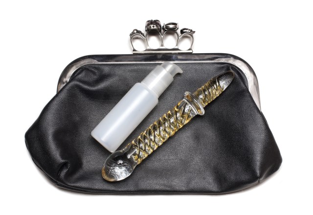a glass dildo and bottle of lube in a nice clutch purse