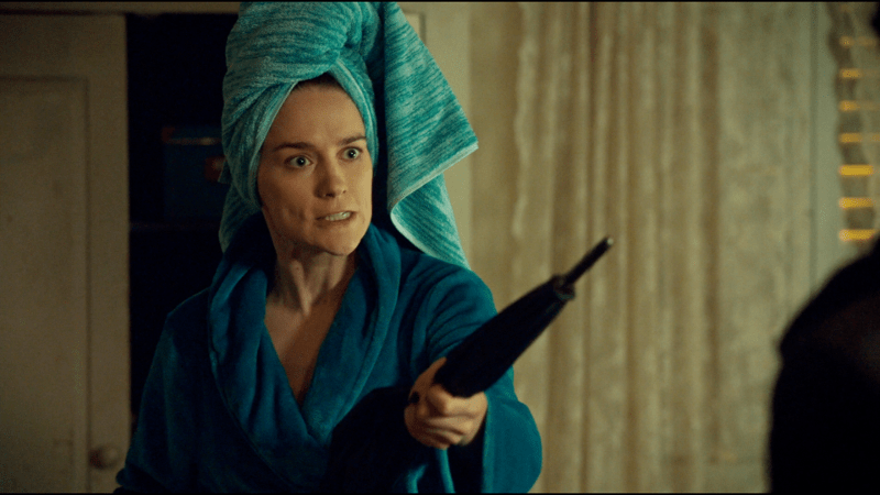 Wynonna with her hair up in a towel wields an umbrella as a weapon 