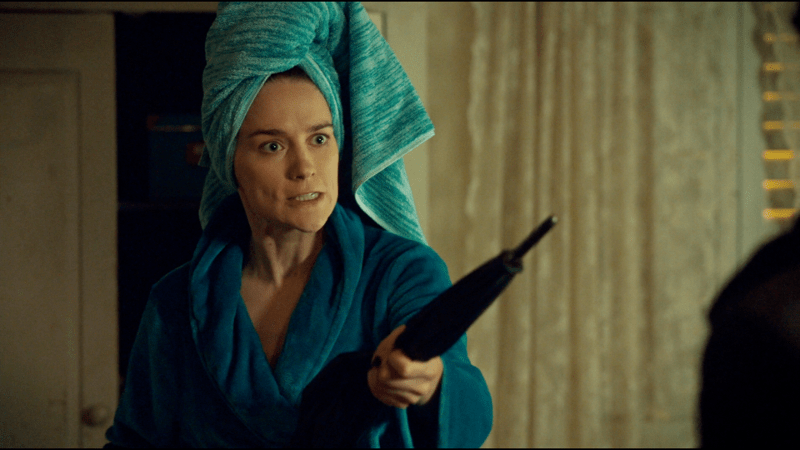 Wynonna with her hair up in a towel wields an umbrella as a weapon