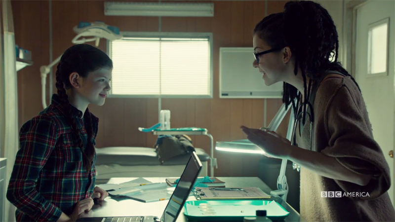 Cosima and Charlotte smile at.each other over a microscope