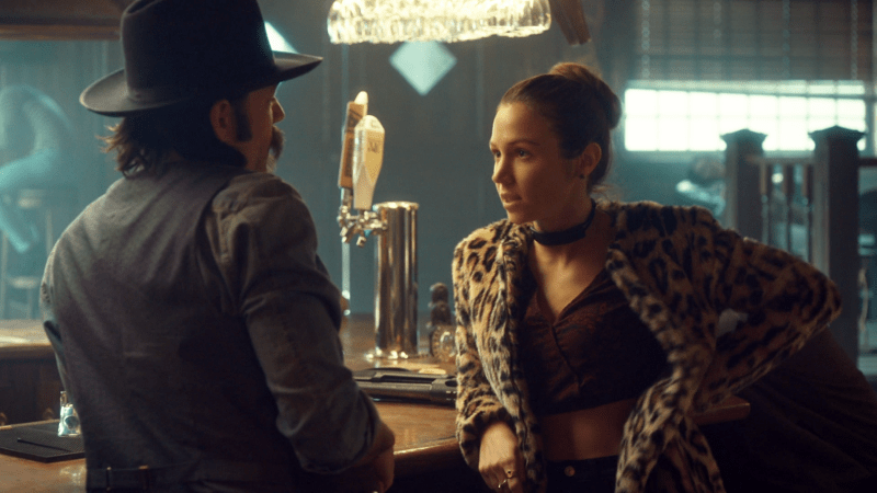 Waverly leans on the bar in her leopard coat talking to Doc in his cowboy hat