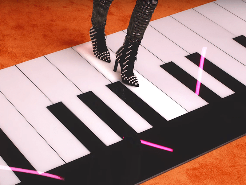 Feet playing a giant piano on the ground, in studded black heels.