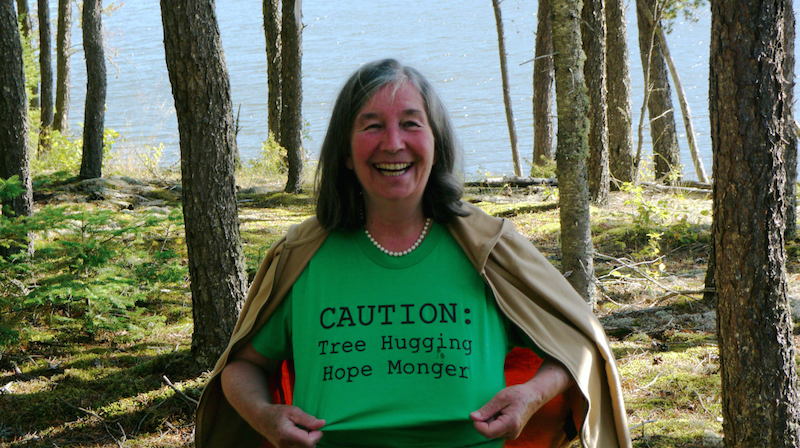 an older white woman wearing a shirt that says "CAUTION: Tree Hugging Hope Monger."