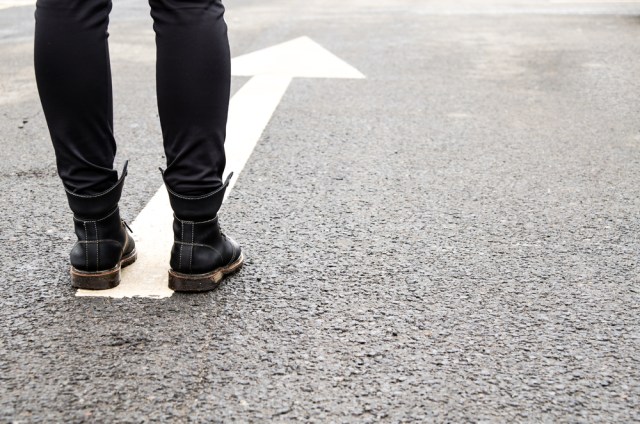 A person wearing black leggings and black boots stands on top of an arrow painted in the street, ready to walk forward.