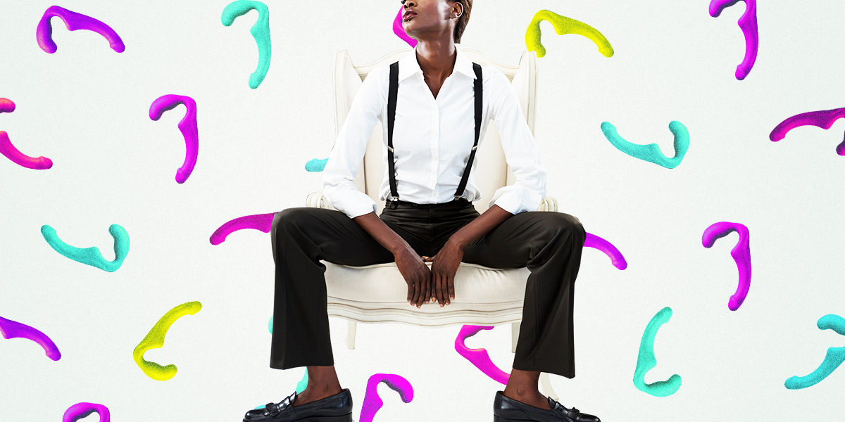 Colorful background of dildos, butch lesbian sitting on a chair casually in suspenders and a white button up shirt