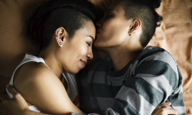 Two Asian women facing each other laying down and cuddling