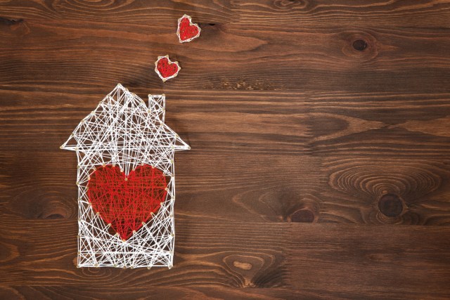 Overhead shot of some white wire made into the shape of a house. There is a red heart in the center of the house, and two smaller red hearts coming from the chimney.