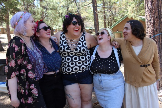 Group of five queer people with their arms around each other, laughing together
