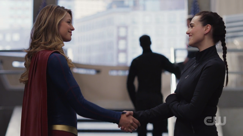 Supergirl and Lena Luthor shake hands while beaming at each other