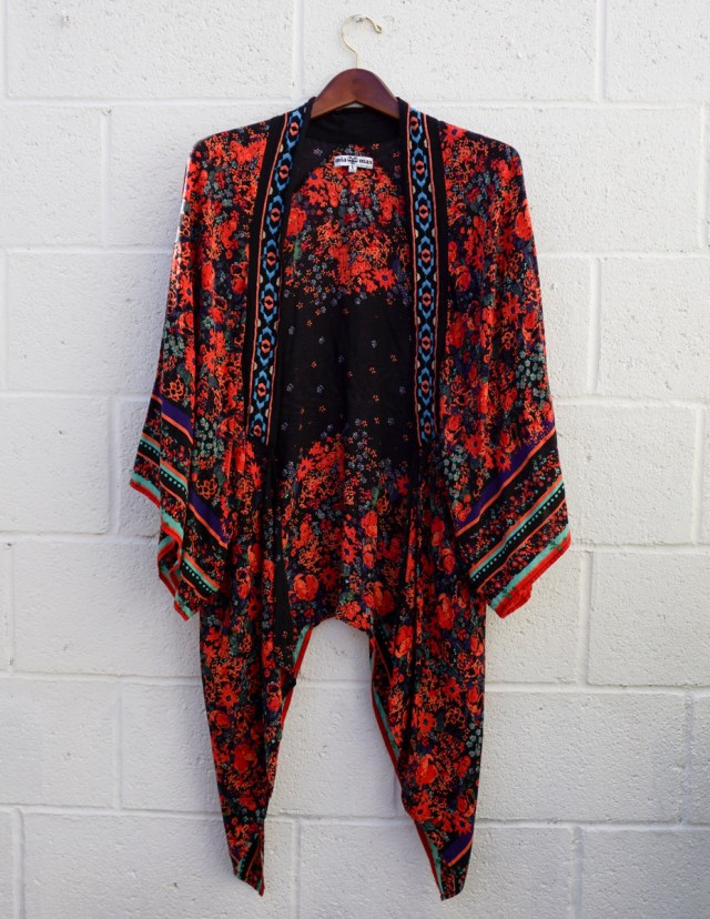 A black kimono-style robe with red floral print and decorative edging, hanging against a white brick wall.