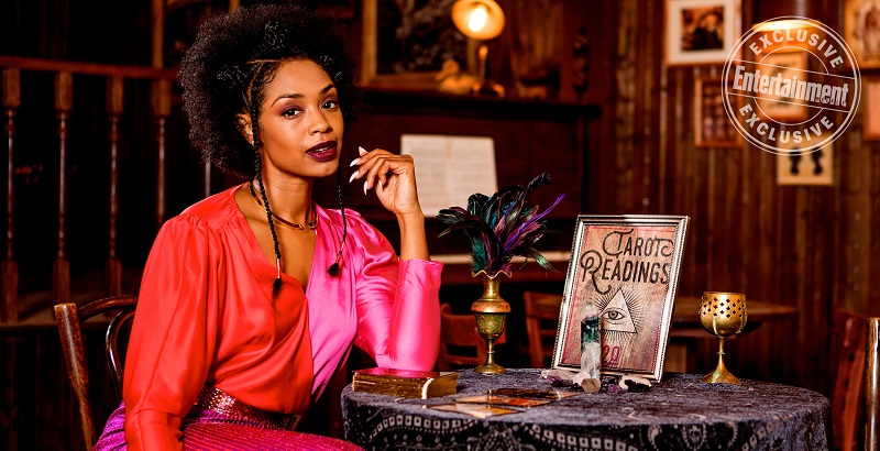 Kate sits at a table with witchy things in front of her 