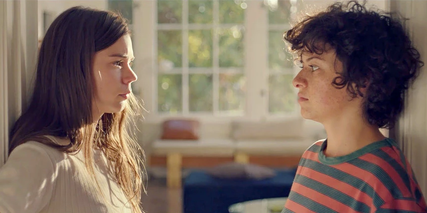 Two girls in lesbian movie "Duck Butter" looking at each other wearily inside a house on a sunny day