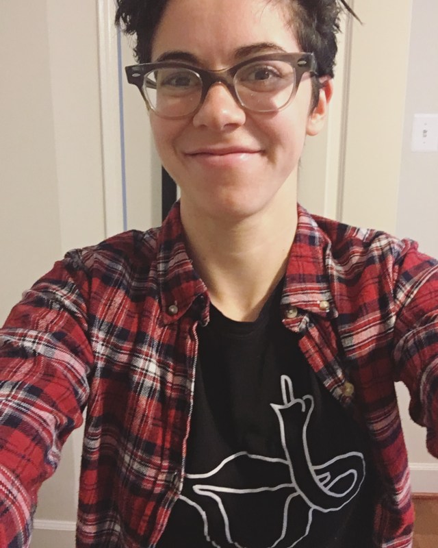 Carrie wearing a red flannel over a shirt with a cartoon uterus giving the middle finger.