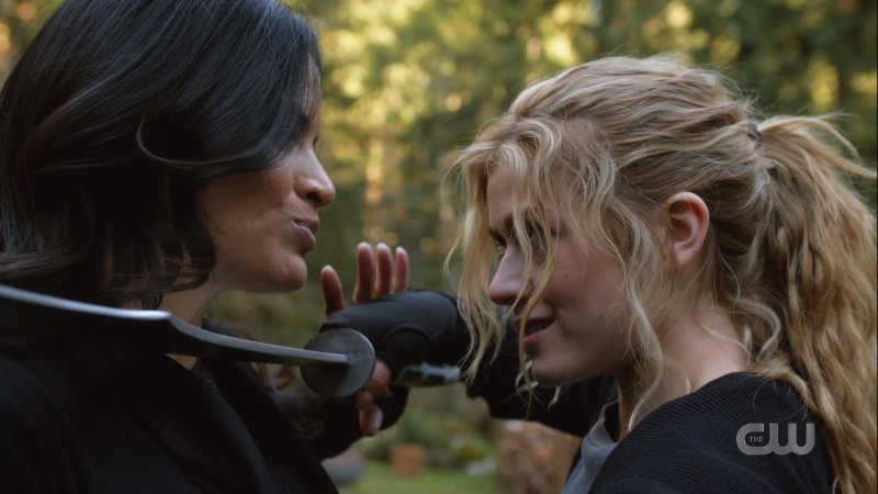 Mia has a sword up to Nyssa's neck during training, both women are smirking