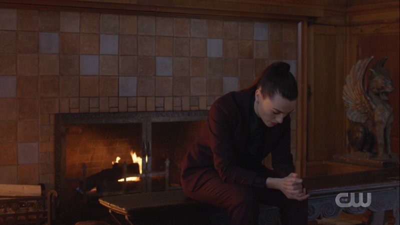 Lena looks distraught and is sitting by the fireplace in her suit