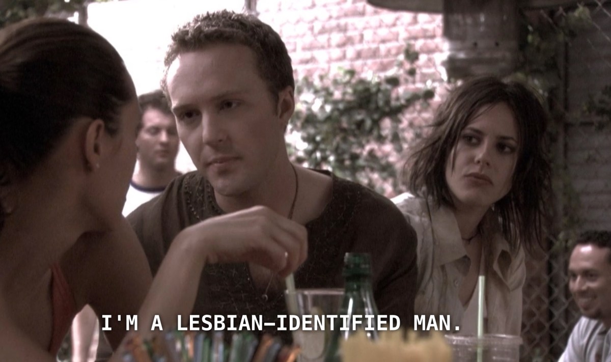 Lisa stares earnestly at Dana, with Shane looking on skeptically in the background. Lisa, who is wearing a brown thermal knit tee and has short brown hair, says to Dana, "I'm a lesbian-identified man."