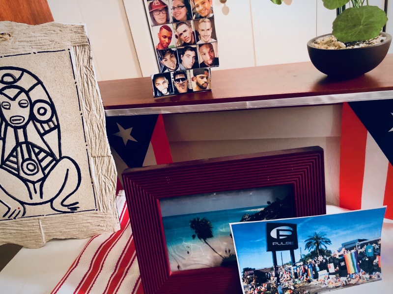 A home photograph of an altar built in a living room with a collection of white table cloth, candles, and Puerto Rican flags. 