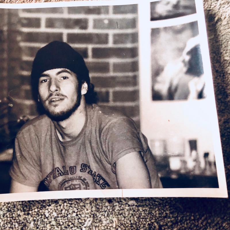 A black-and-white photograph of a gay Puerto Rican man in the 1970s against a textured background